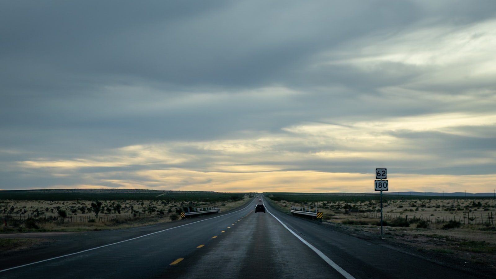 A vehicle on an open highway at dusk beside a US 62 and 180 route marker