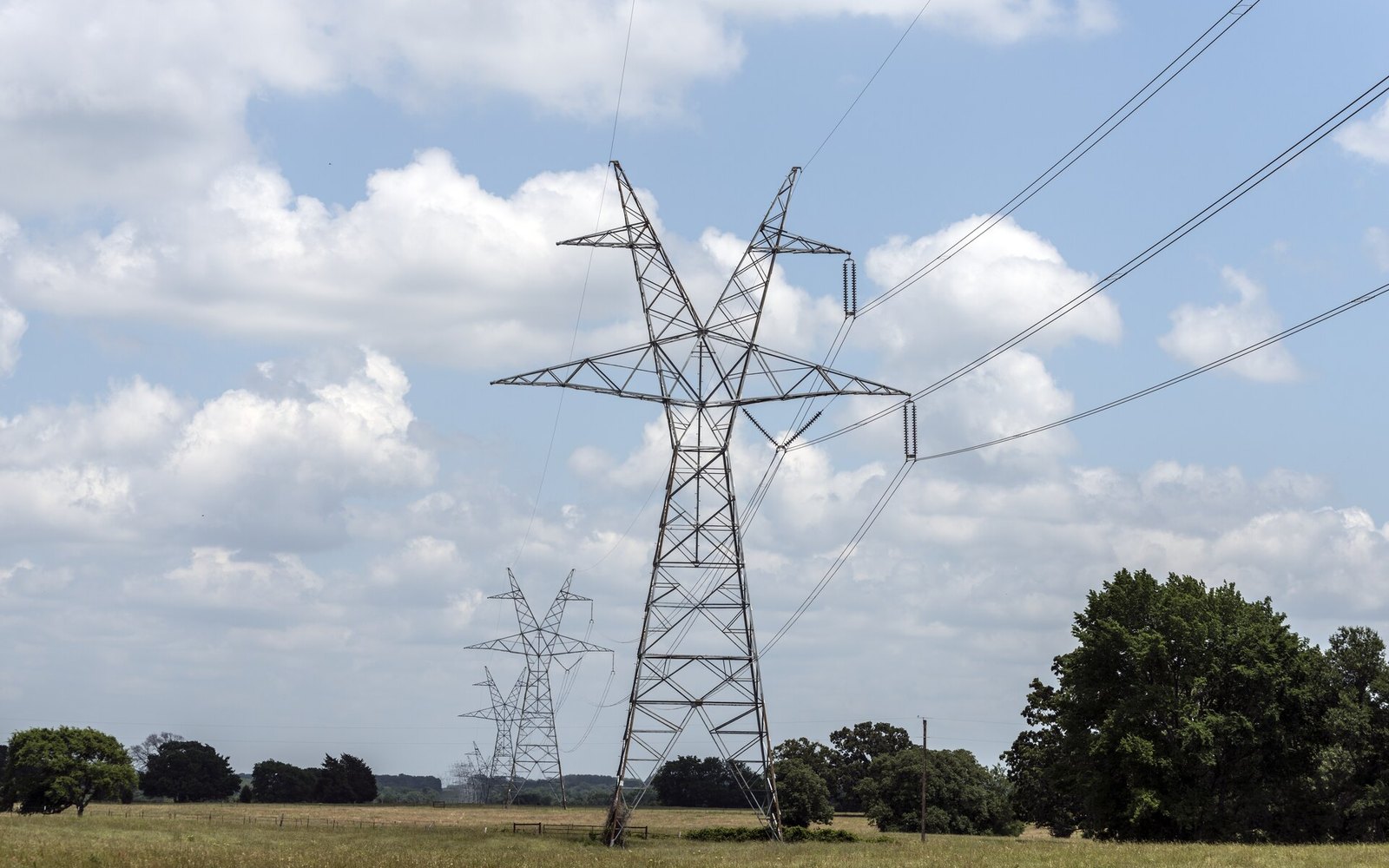 A steel lattice electricity transmission tower carrying power lines against a cloudy sky